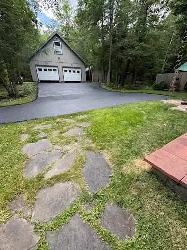Stone path through a grassy yard leading to a detached garage with two white doors, surrounded by trees.