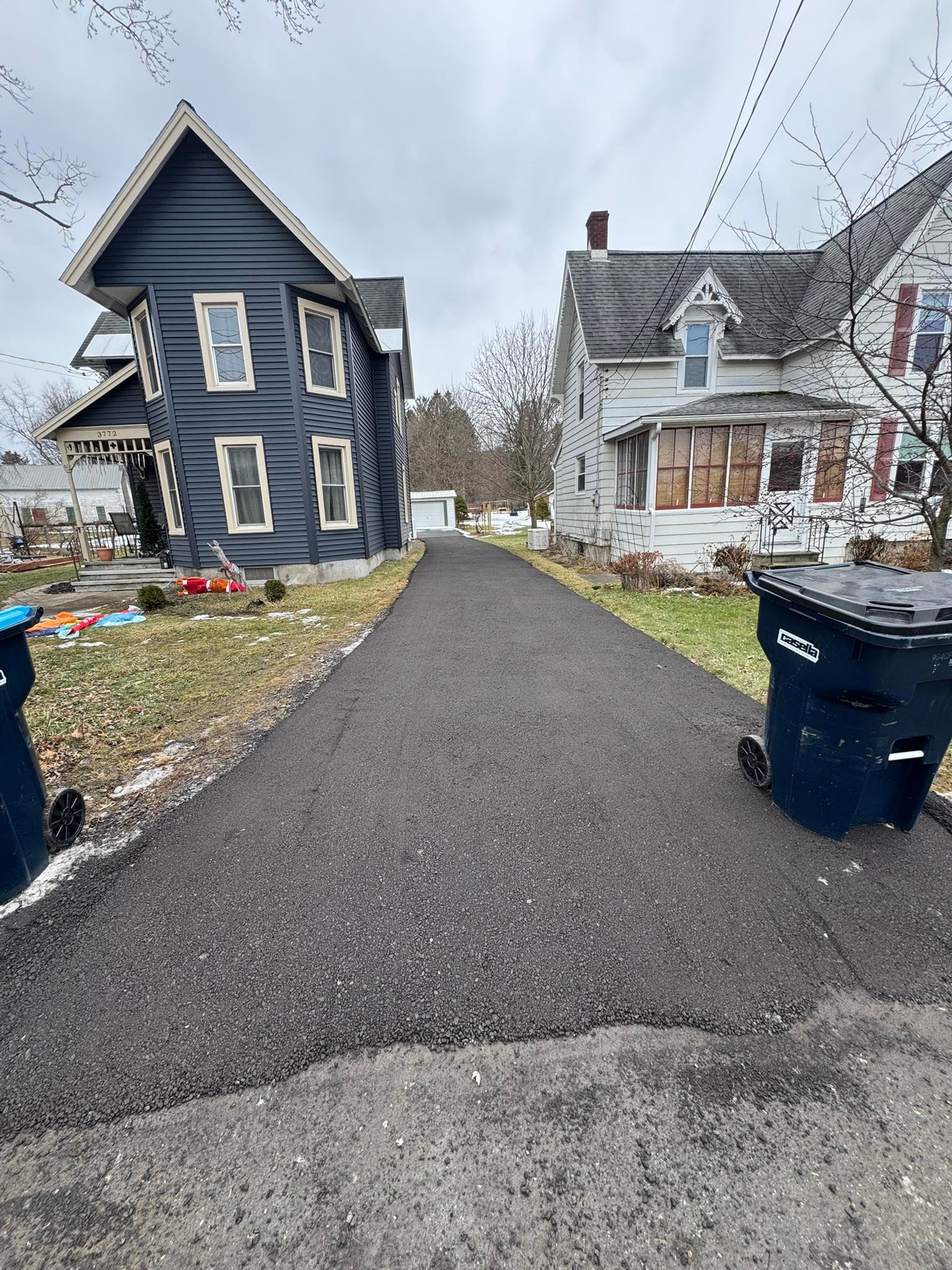 Narrow paved alley between two old houses, with trash bins and scattered debris on both sides.