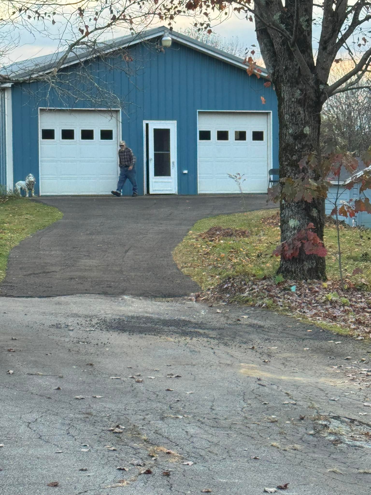 Blue detached garage with two white doors and a person standing in the center doorway, viewed from a driveway.