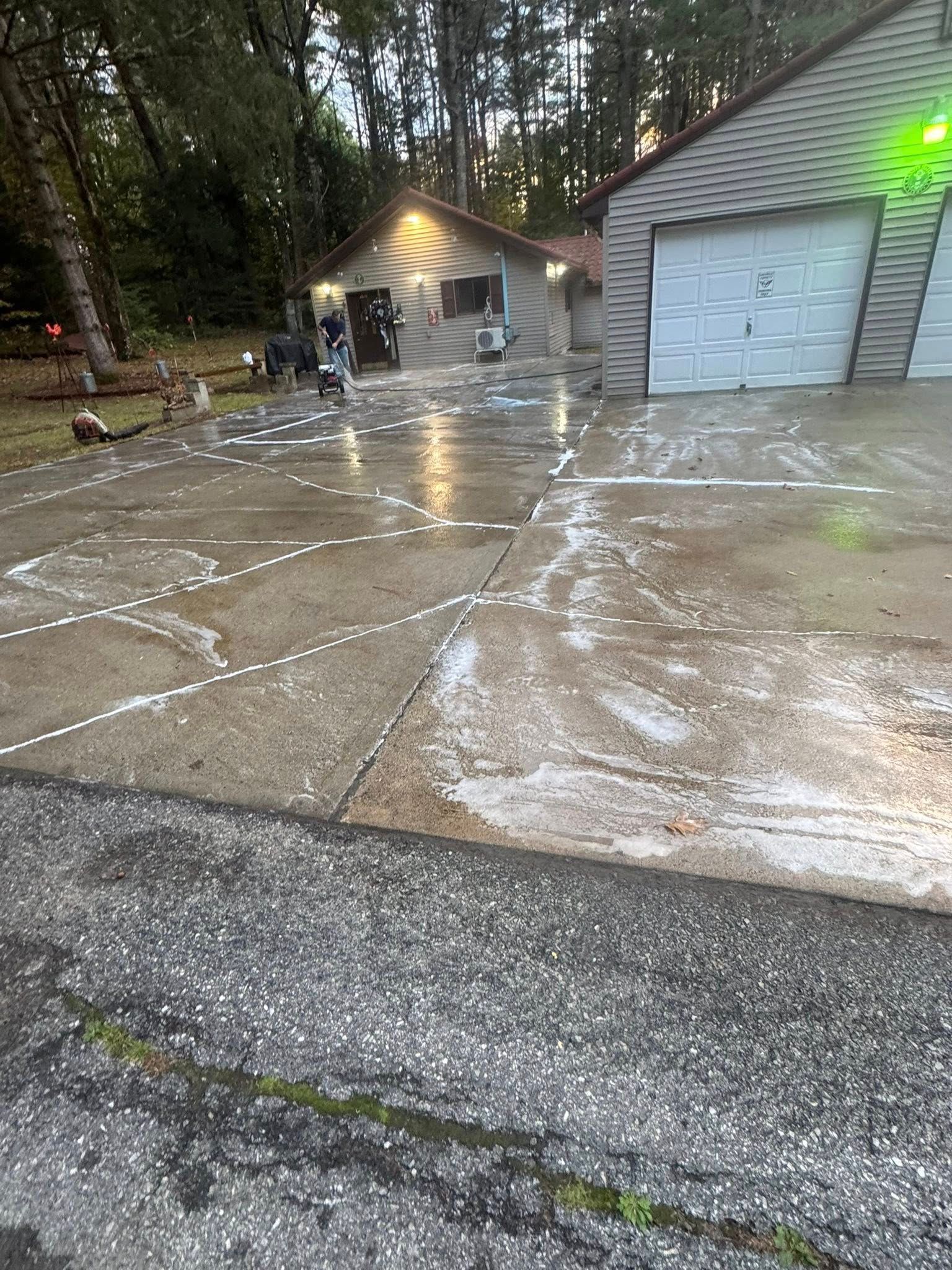 Wet driveway and garage in a wooded neighborhood, with water flowing across the concrete after rain.