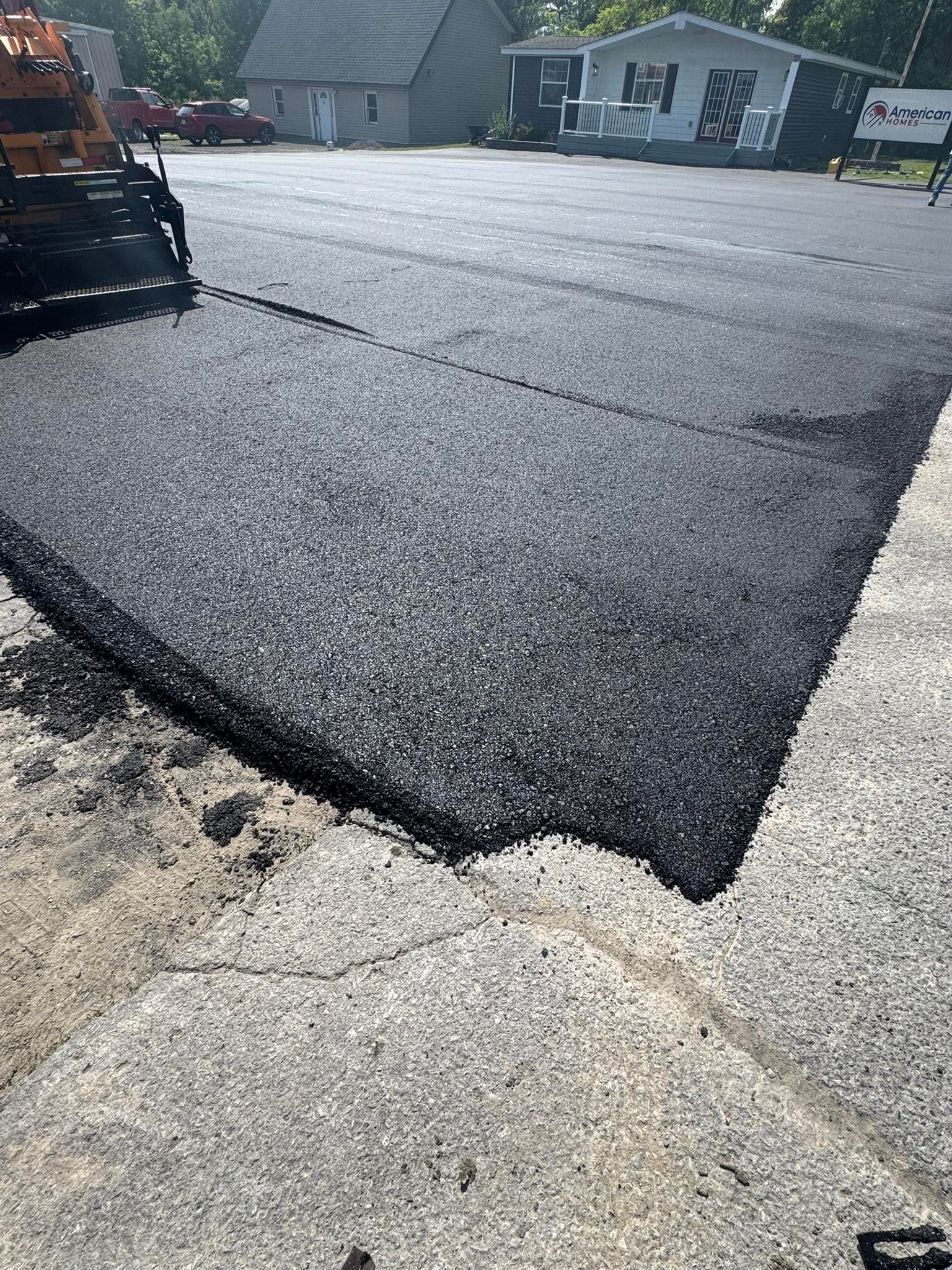 Fresh black asphalt paving at a driveway edge beside a concrete sidewalk and suburban houses