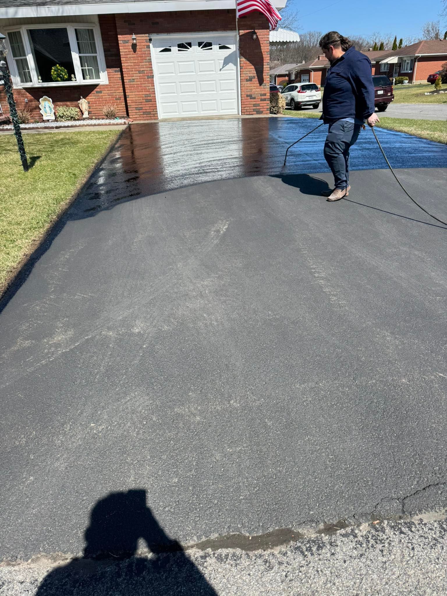 Person standing on a newly paved driveway beside a brick house on a sunny day
