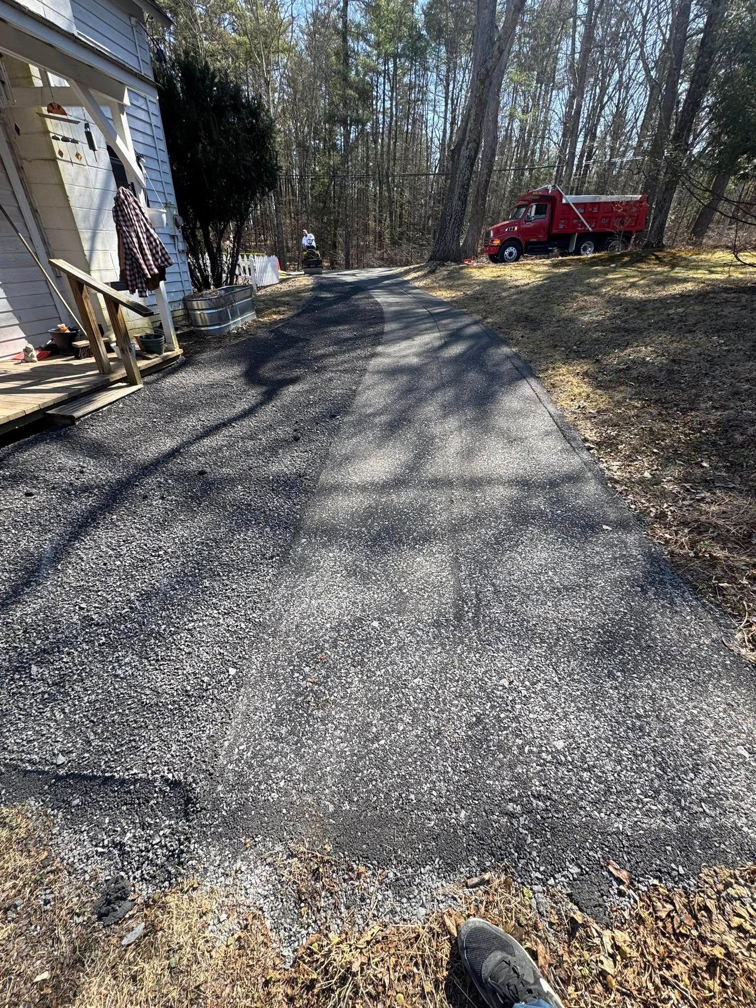 Gravel driveway beside a house, leading into a wooded yard with a red truck parked at the top.