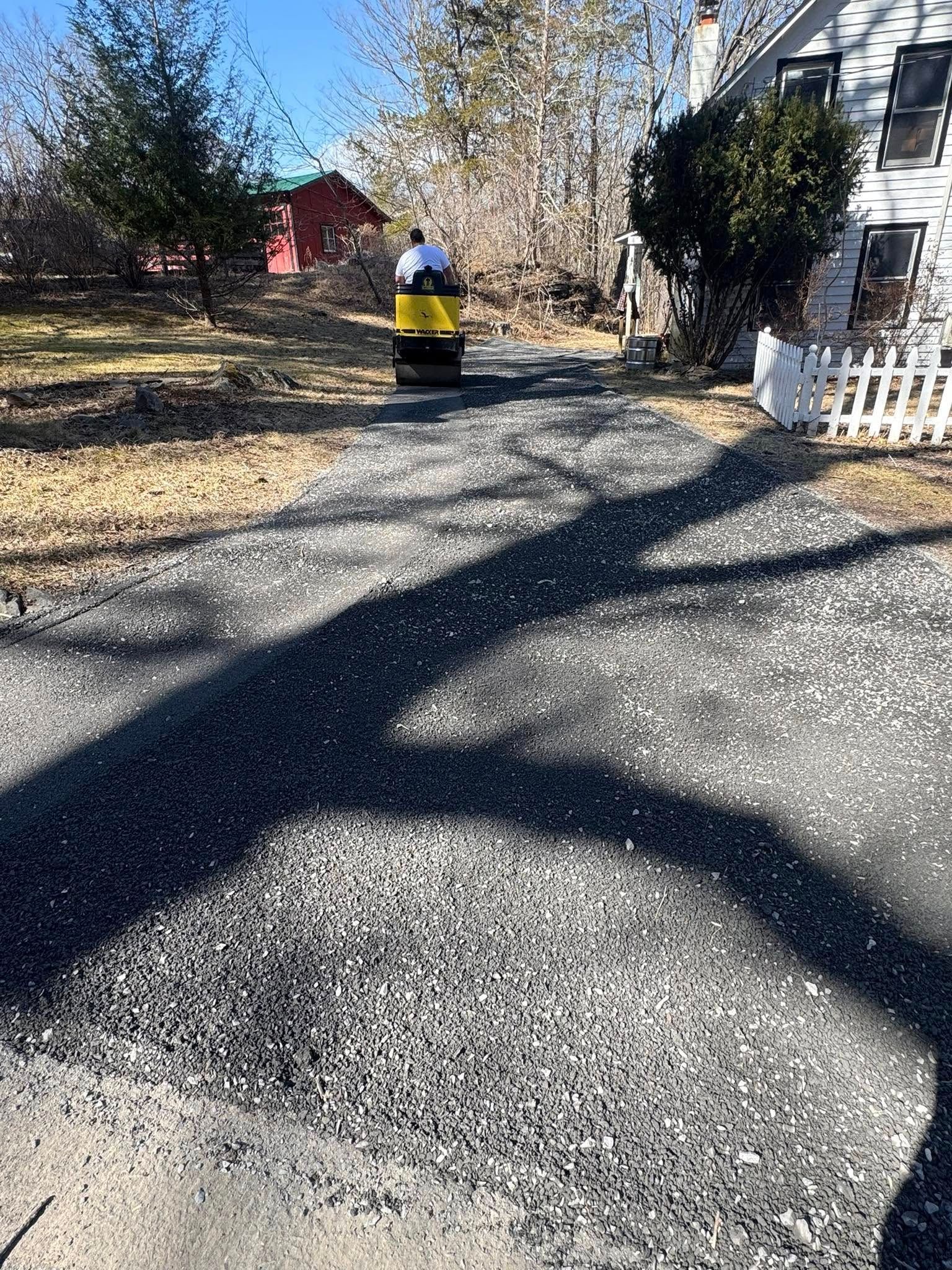 Person in a yellow jacket walking on a gravel driveway near houses and trees.