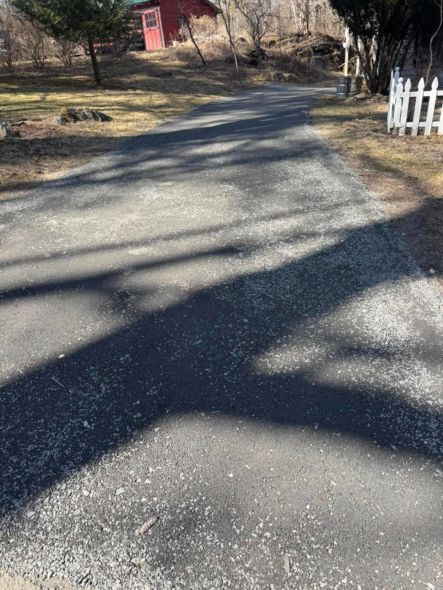 Gravel driveway with tree shadows, a red mailbox, and a white fence in the background