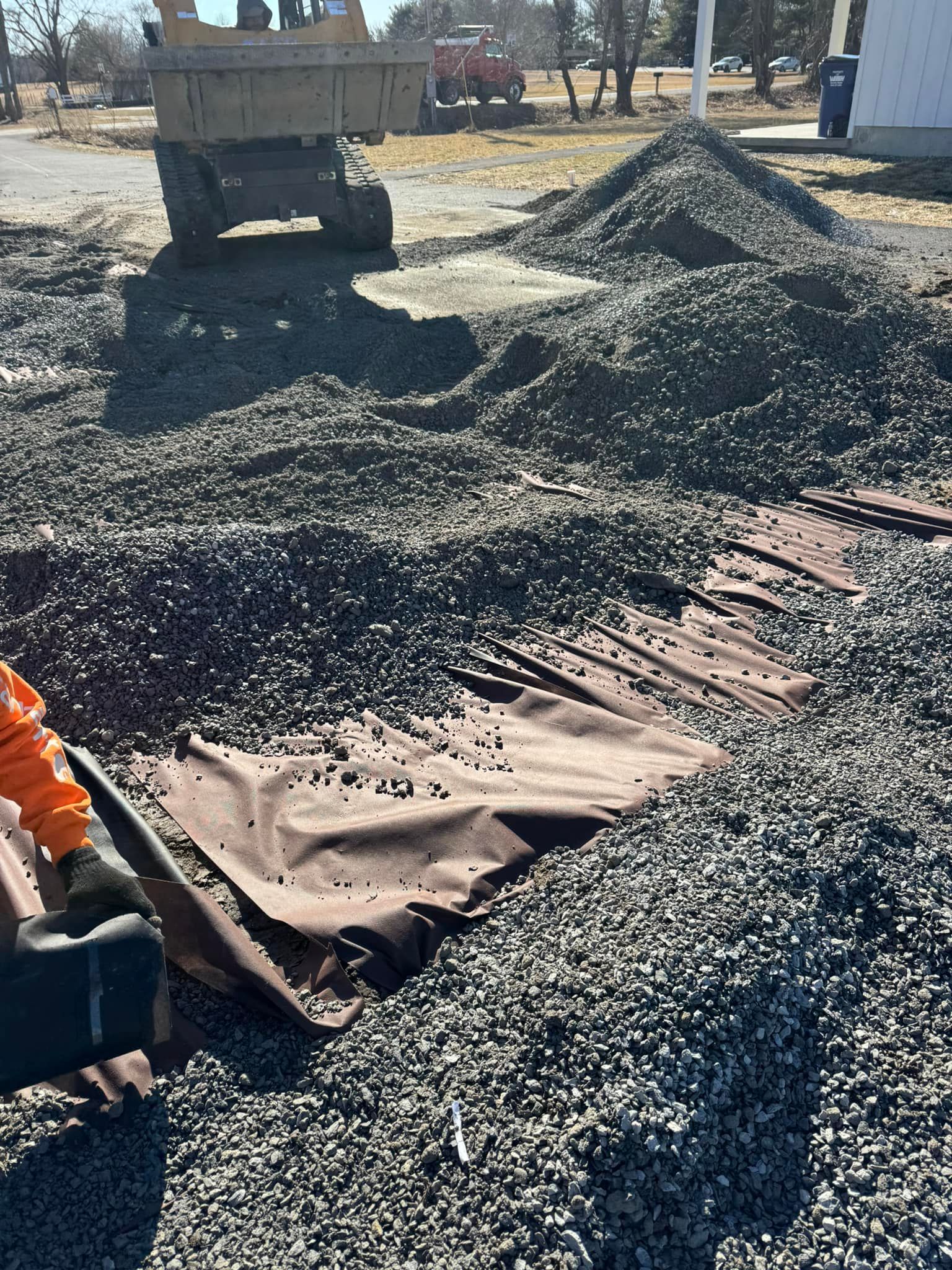 Construction site with gravel piles, a dump truck, and workers spreading black tarp