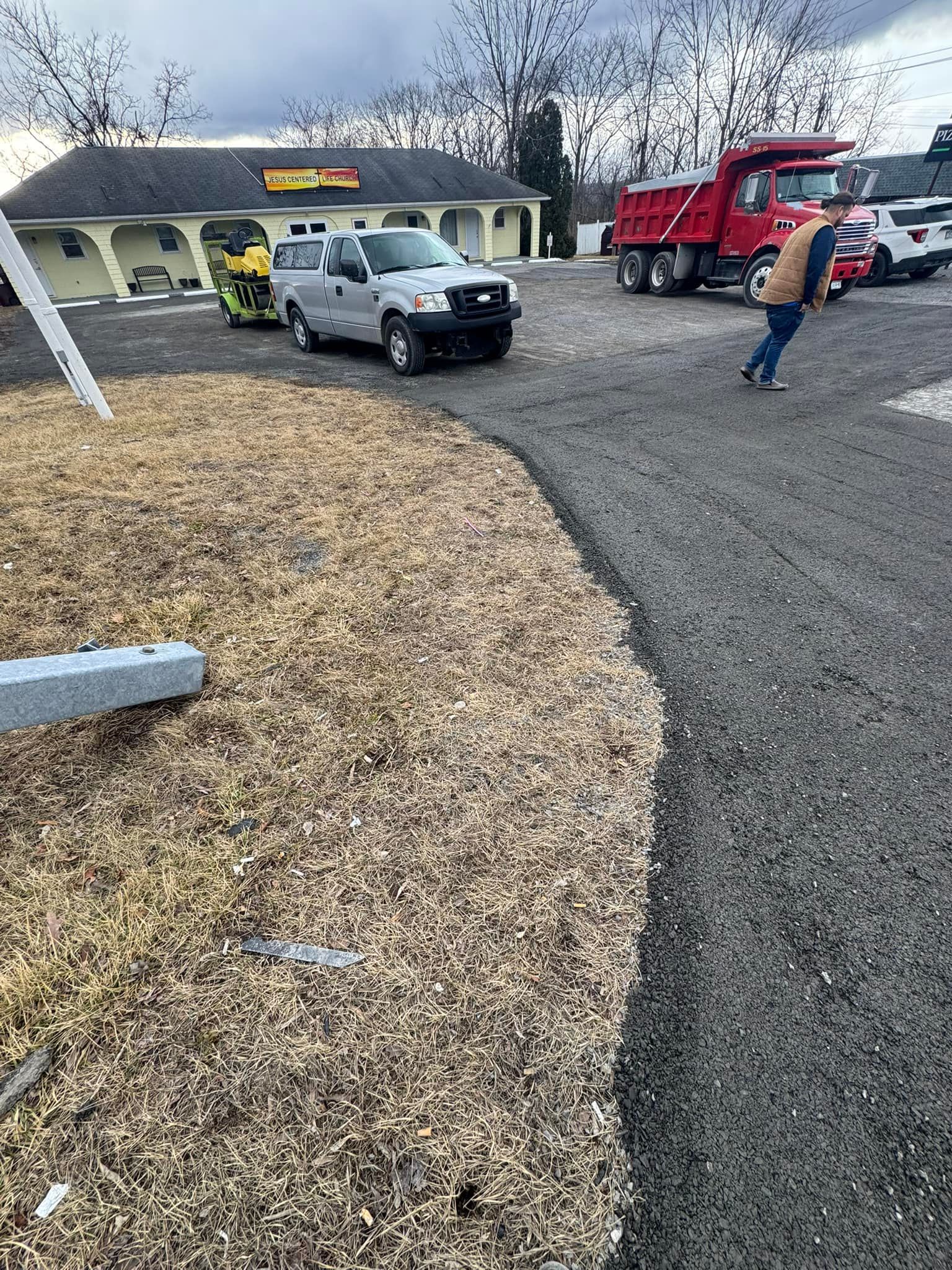 Truck, SUV, and worker outside a building on a gravel lot under a gray sky.