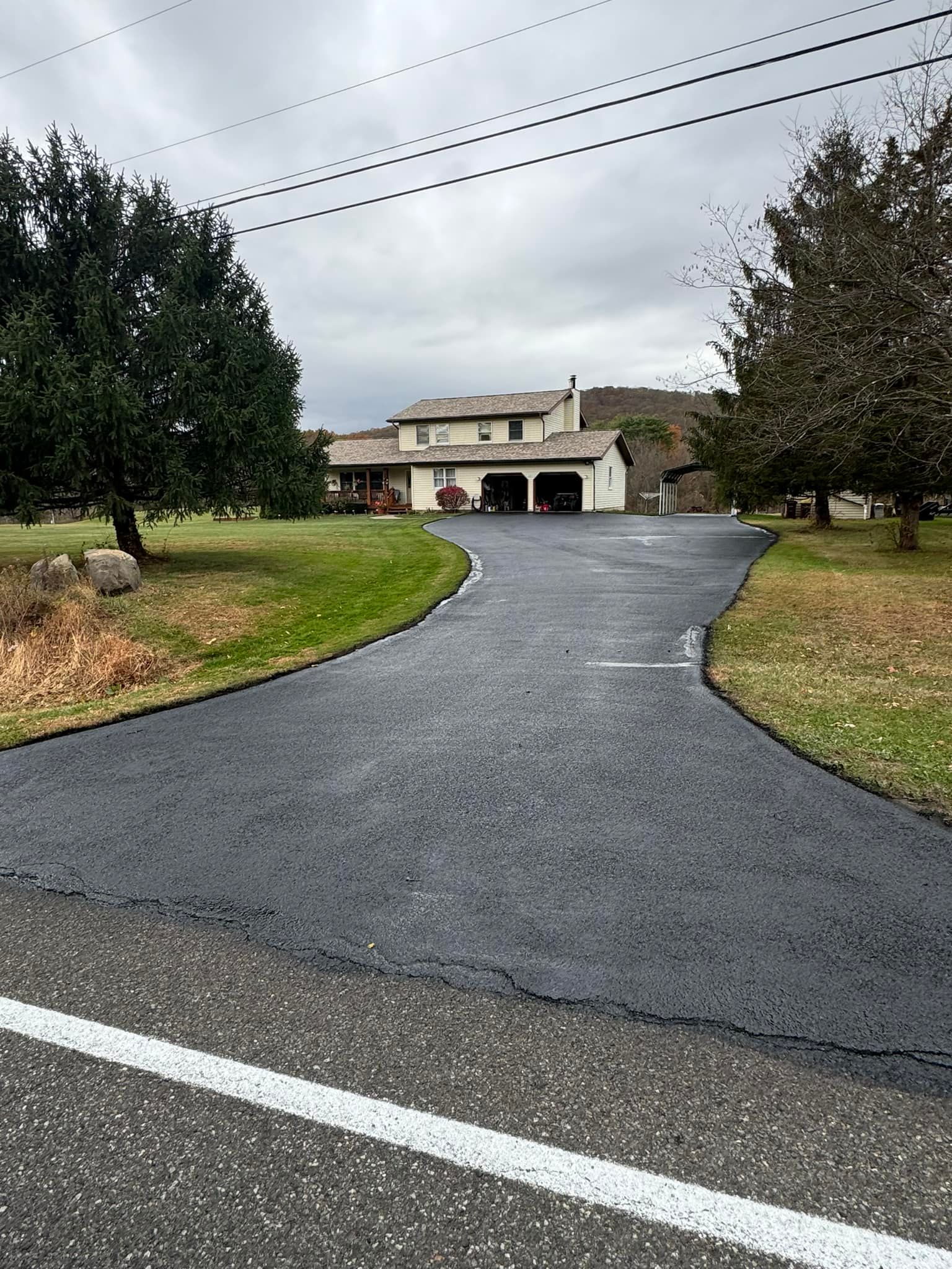 Curved driveway leading to a beige house with trees and overcast sky overhead