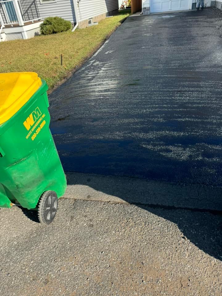 Green trash bin on a driveway beside a freshly paved black asphalt road.