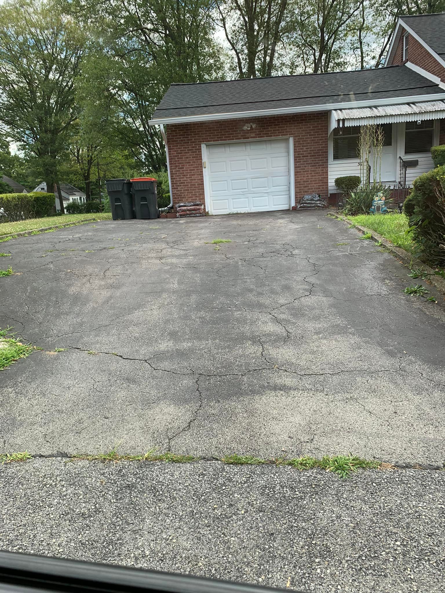 Brick house with a white garage door, wide paved driveway, and trees in the background