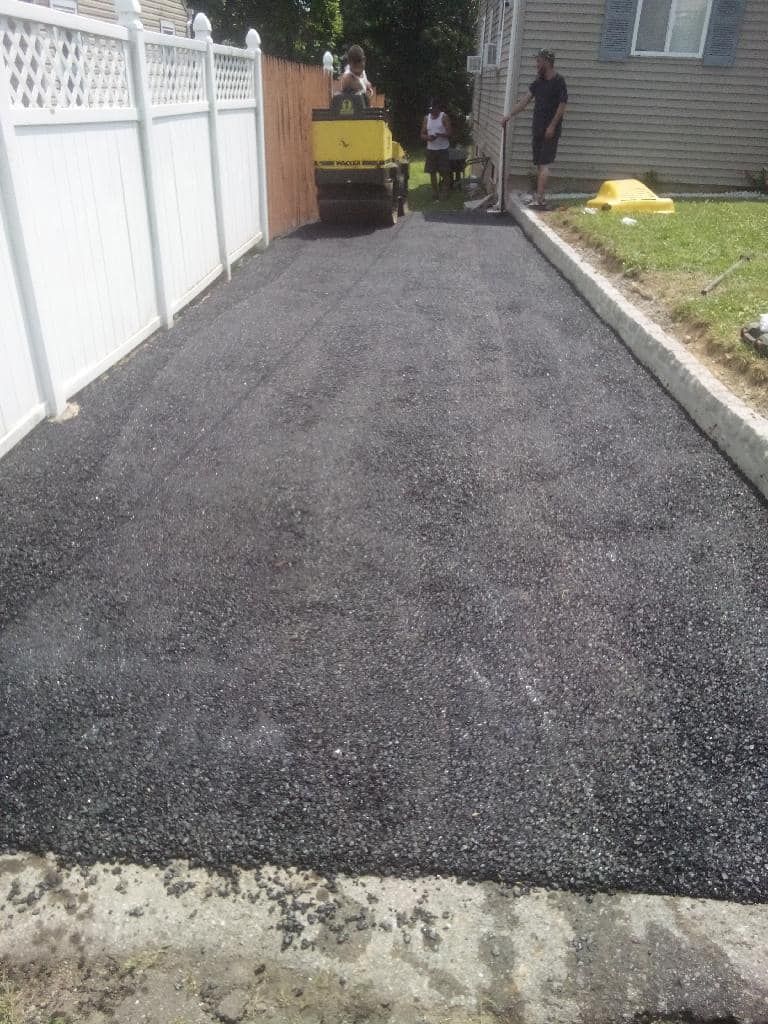 Fresh black gravel driveway beside a white fence, with workers and a yellow machine at the far end
