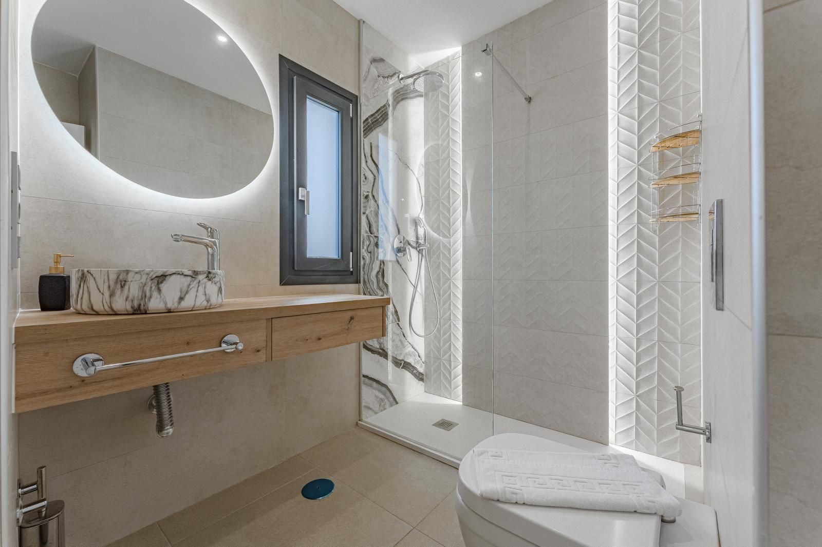 Baño moderno con espejo redondo, lavabo de madera, ducha a ras de suelo e inodoro.