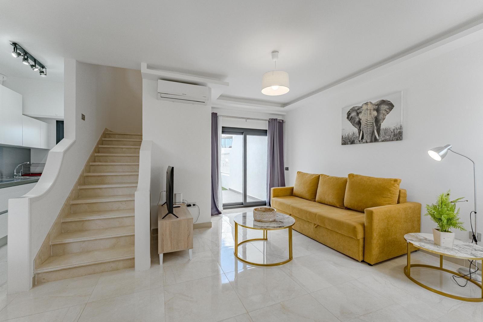 Habitación doble luminosa con cabeceros beige, colchas color mostaza y una pequeña mesita de noche blanca.