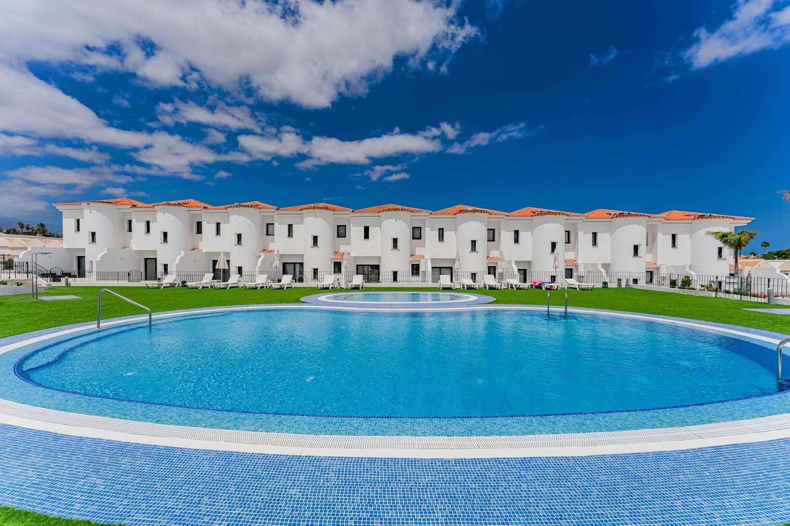 Hilera de casas adosadas blancas junto a una gran piscina azul bajo un cielo brillante.