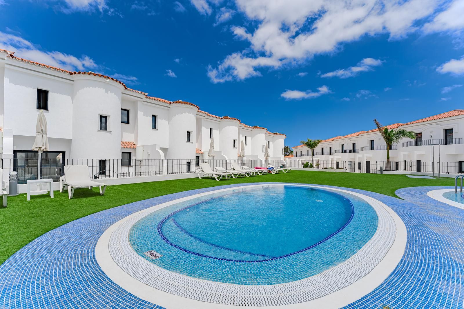 Edificios de apartamentos blancos, una piscina de mosaico azul bajo un cielo brillante