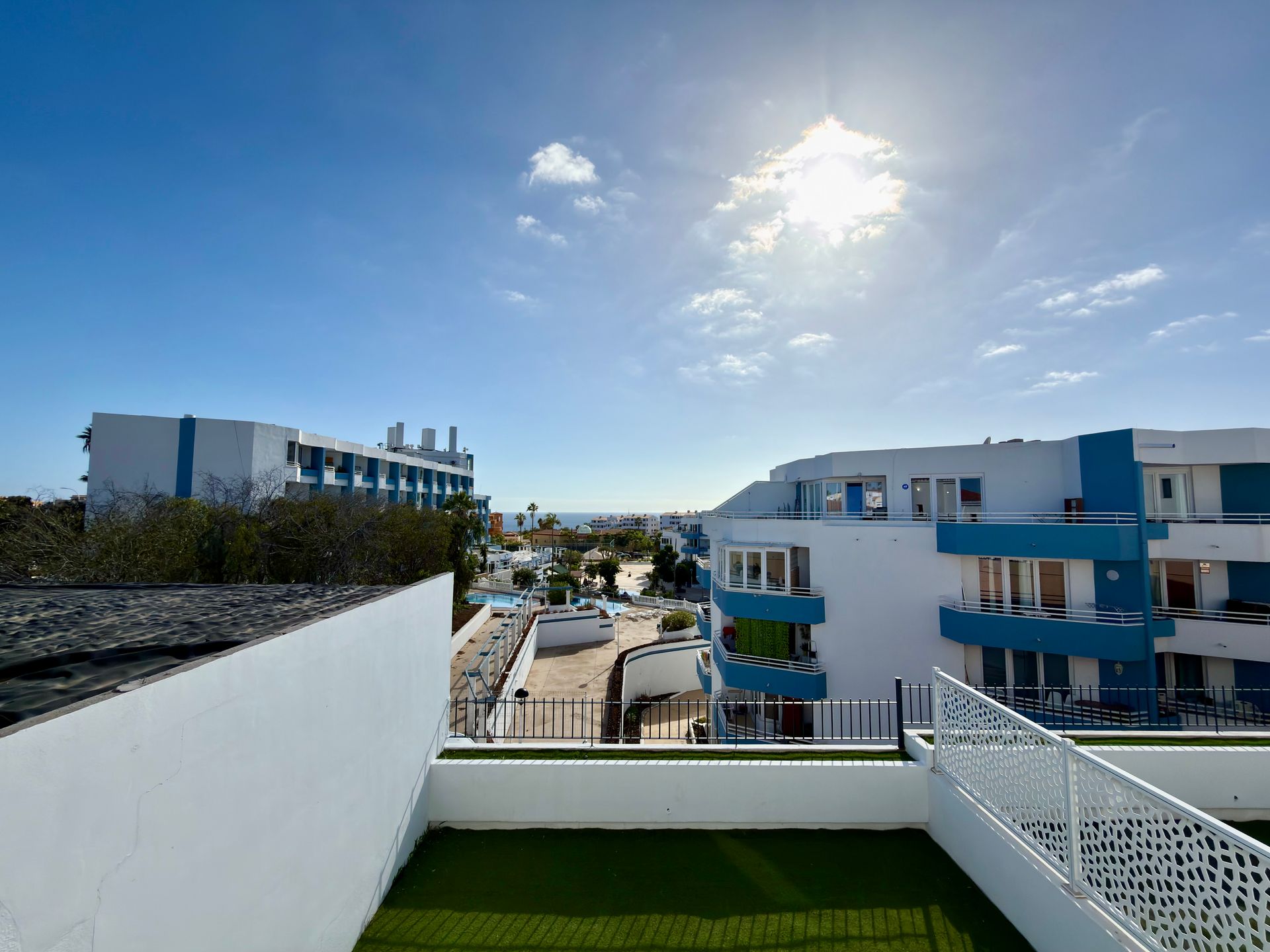 Terraza soleada en la azotea con paredes blancas, césped verde, edificios de apartamentos azules y un cielo brillante.