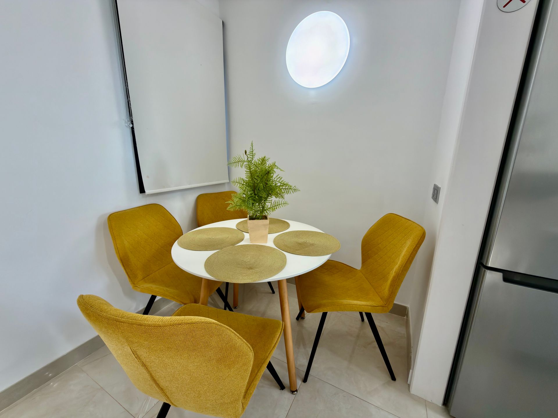 Mesa redonda pequeña con cuatro sillas de color amarillo mostaza en una habitación moderna y luminosa.