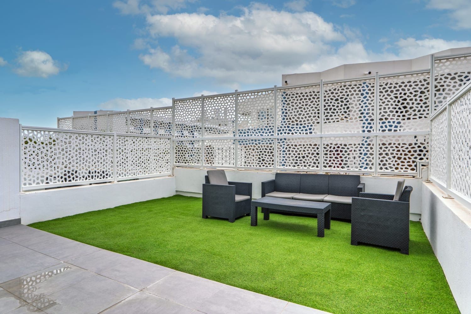 Terraza privada en la azotea con césped artificial, cómodos asientos de mimbre y pantallas decorativas blancas.