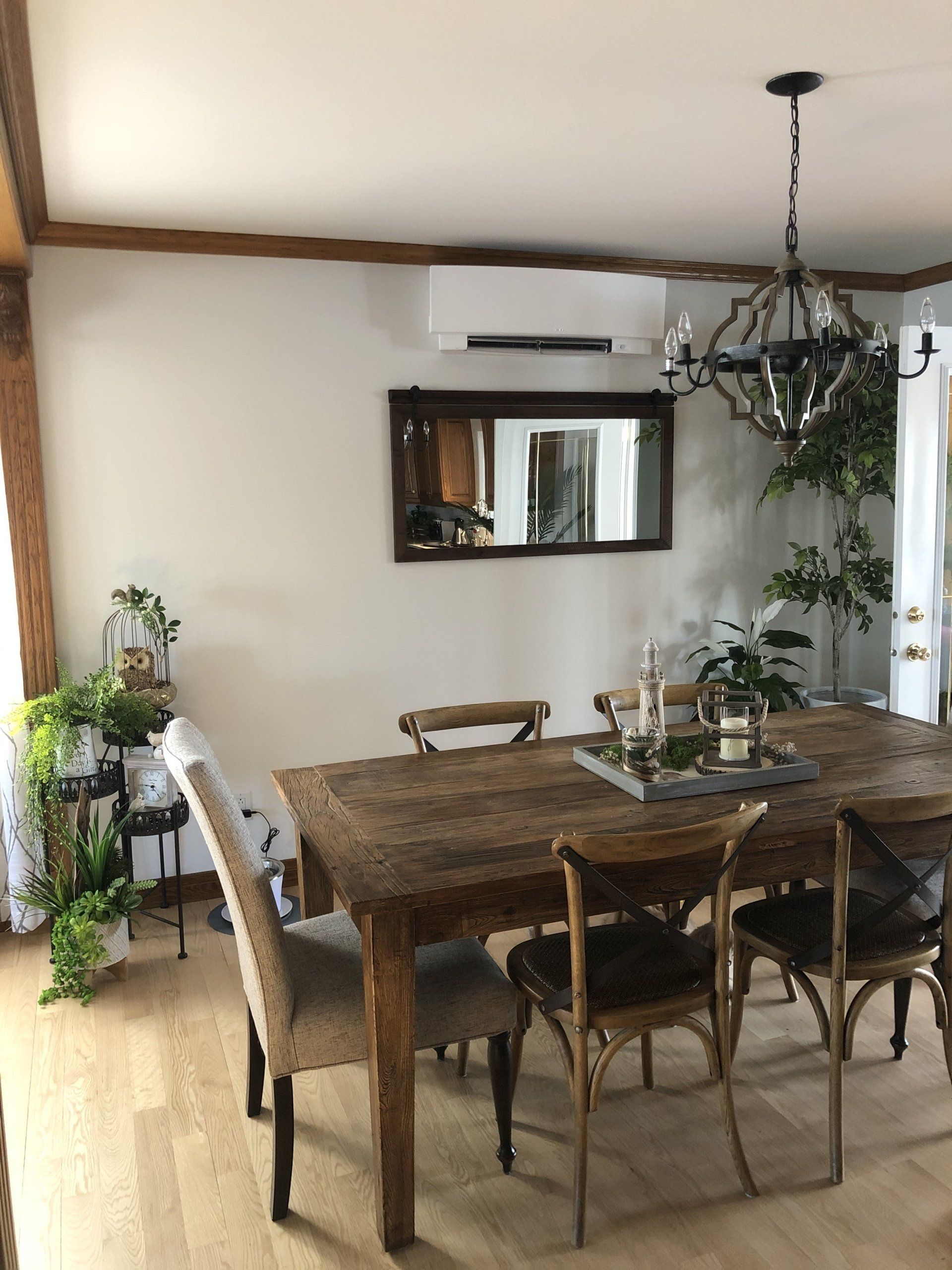 Salle à manger avec table en bois, chaises, miroir, lustre et plantes.