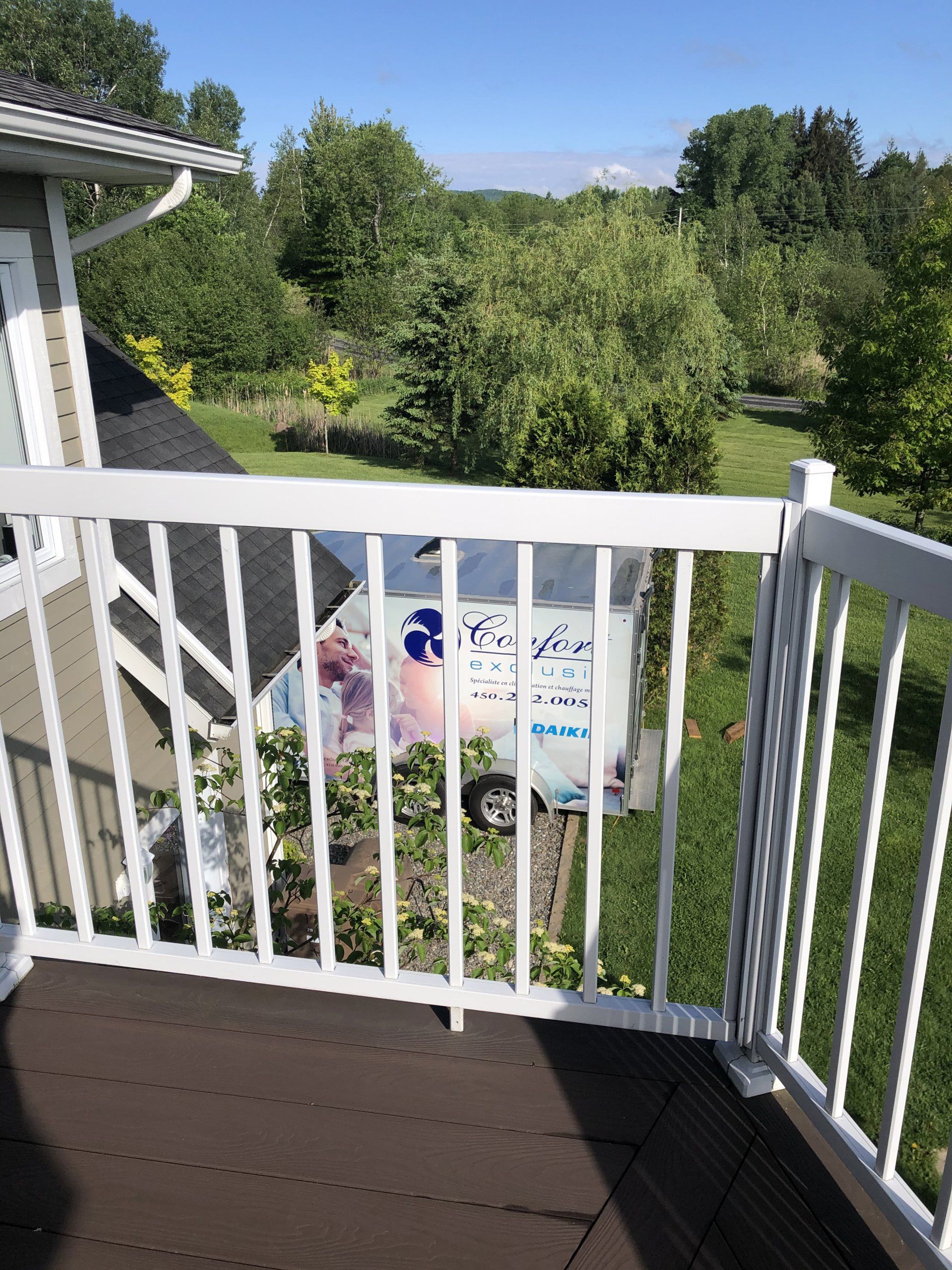 Vue depuis une balustrade blanche sur un food truck bleu clair, installé dans une cour verdoyante arborée.