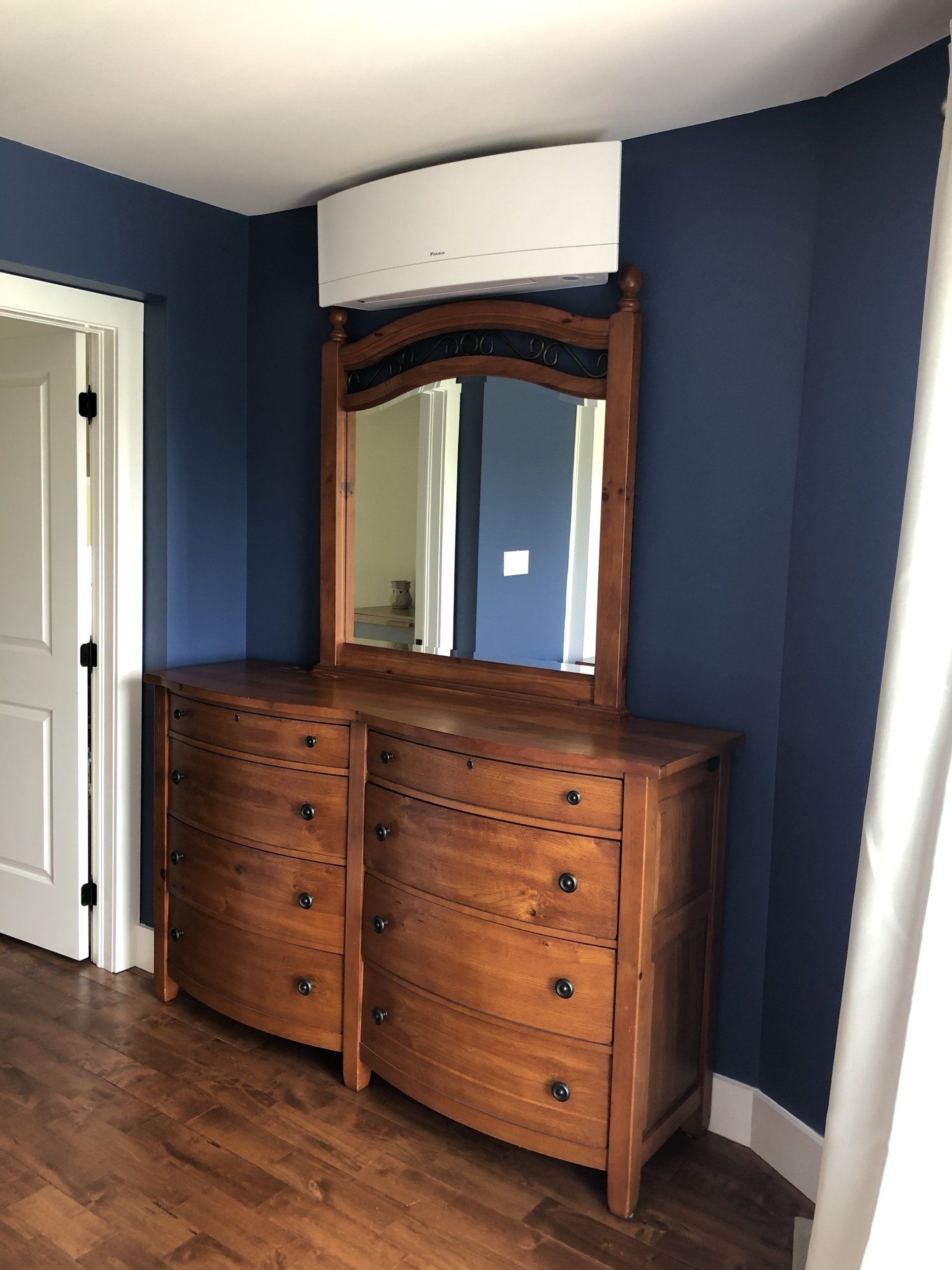 Commode en bois avec miroir contre un mur bleu foncé ; climatiseur blanc au-dessus.