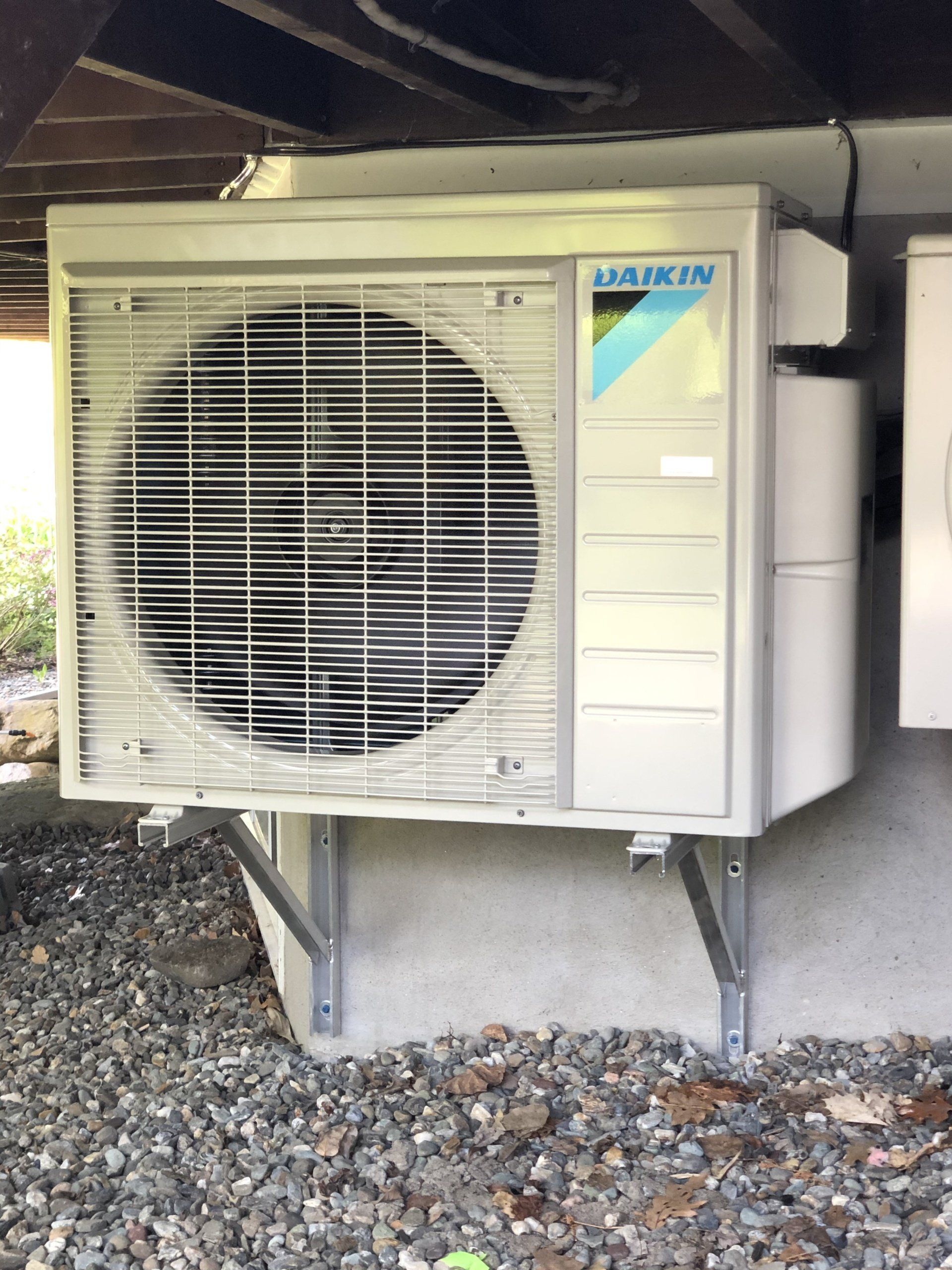 Unité de climatisation Daikin montée sur une base en béton sous un bâtiment, entourée de gravier.