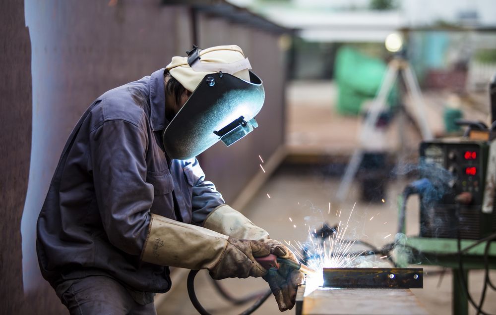Welder in Protective Gear Welding Metal — Cairns Electrical Rewinds & Repairs In Bungalow, QLD