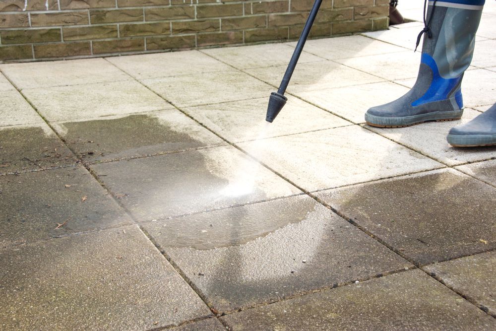 Person power washing a stone patio with a pressure washer, cleaning the surface — Cairns Electrical Rewinds & Repairs In Bungalow, QLD