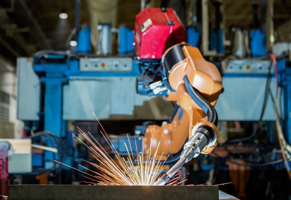 Orange Robotic Arm Welding Metal With Sparks in a Factory Setting — Cairns Electrical Rewinds & Repairs In Bungalow, QLD