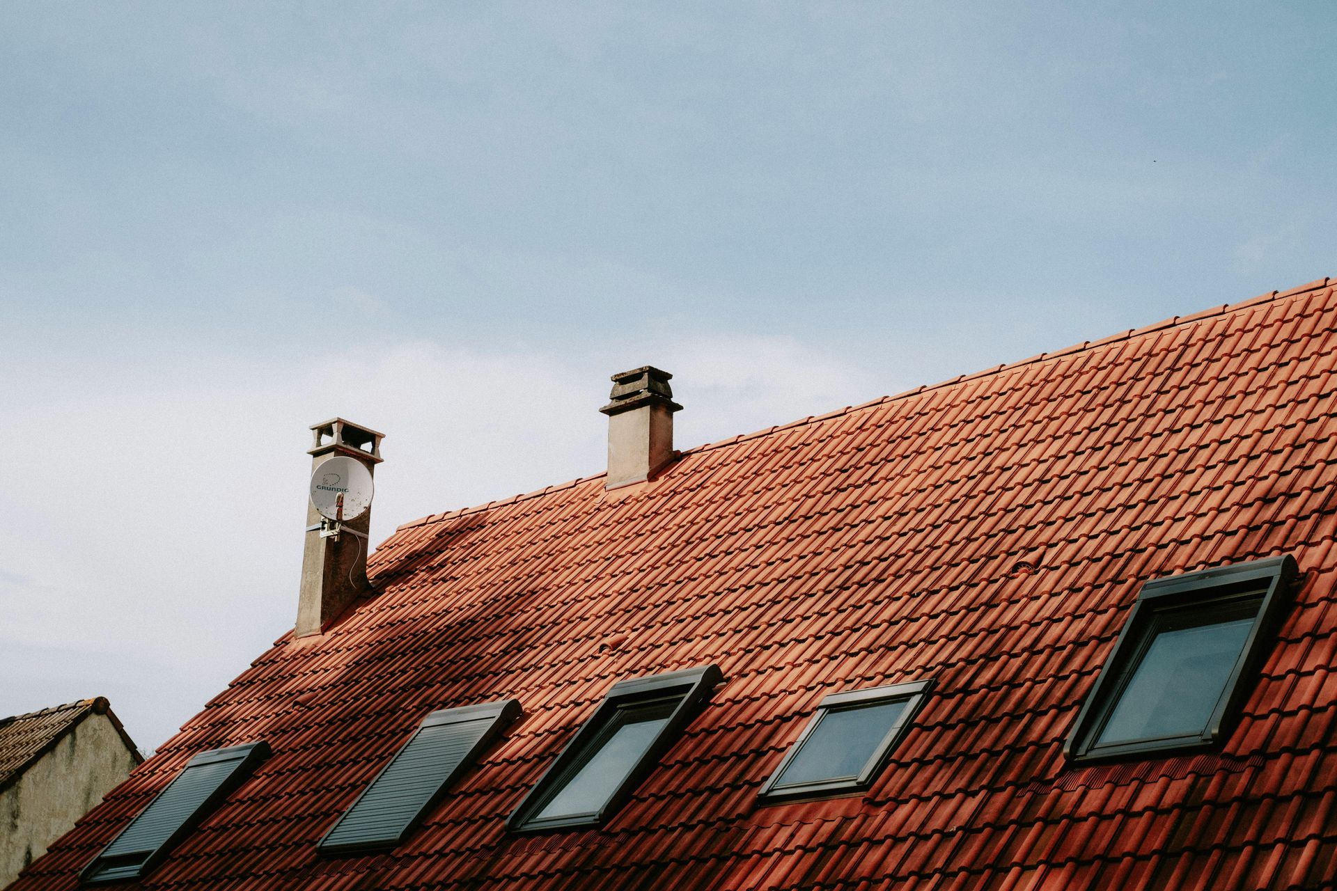 Red tiled roof with skylights and chimneys against a cloudy sky