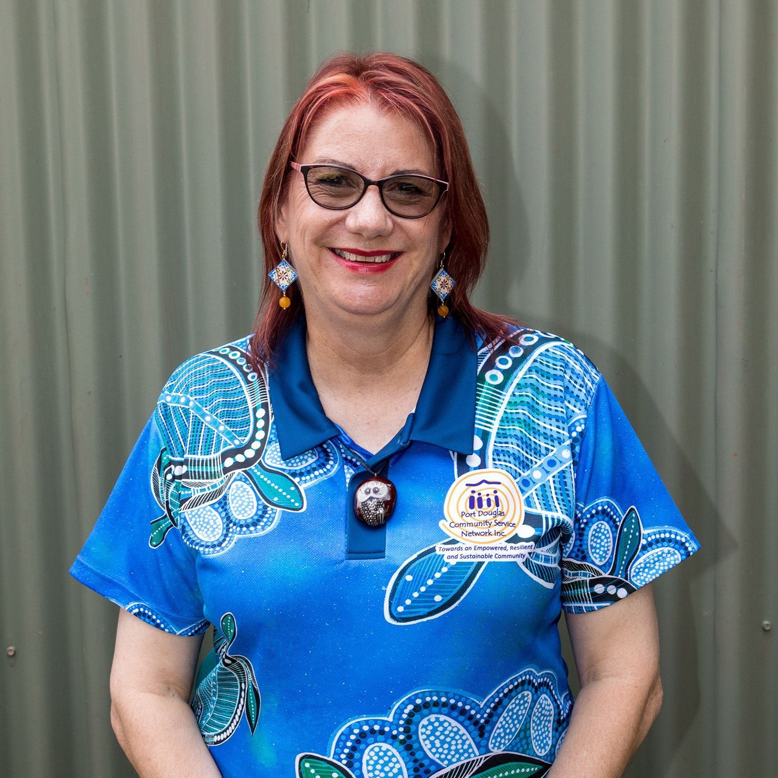 A woman wearing glasses and a blue shirt is standing in front of a wall.