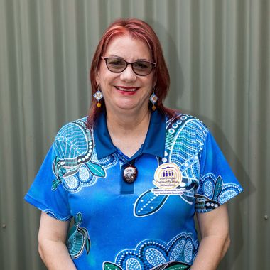 A woman wearing glasses and a blue shirt is standing in front of a wall.