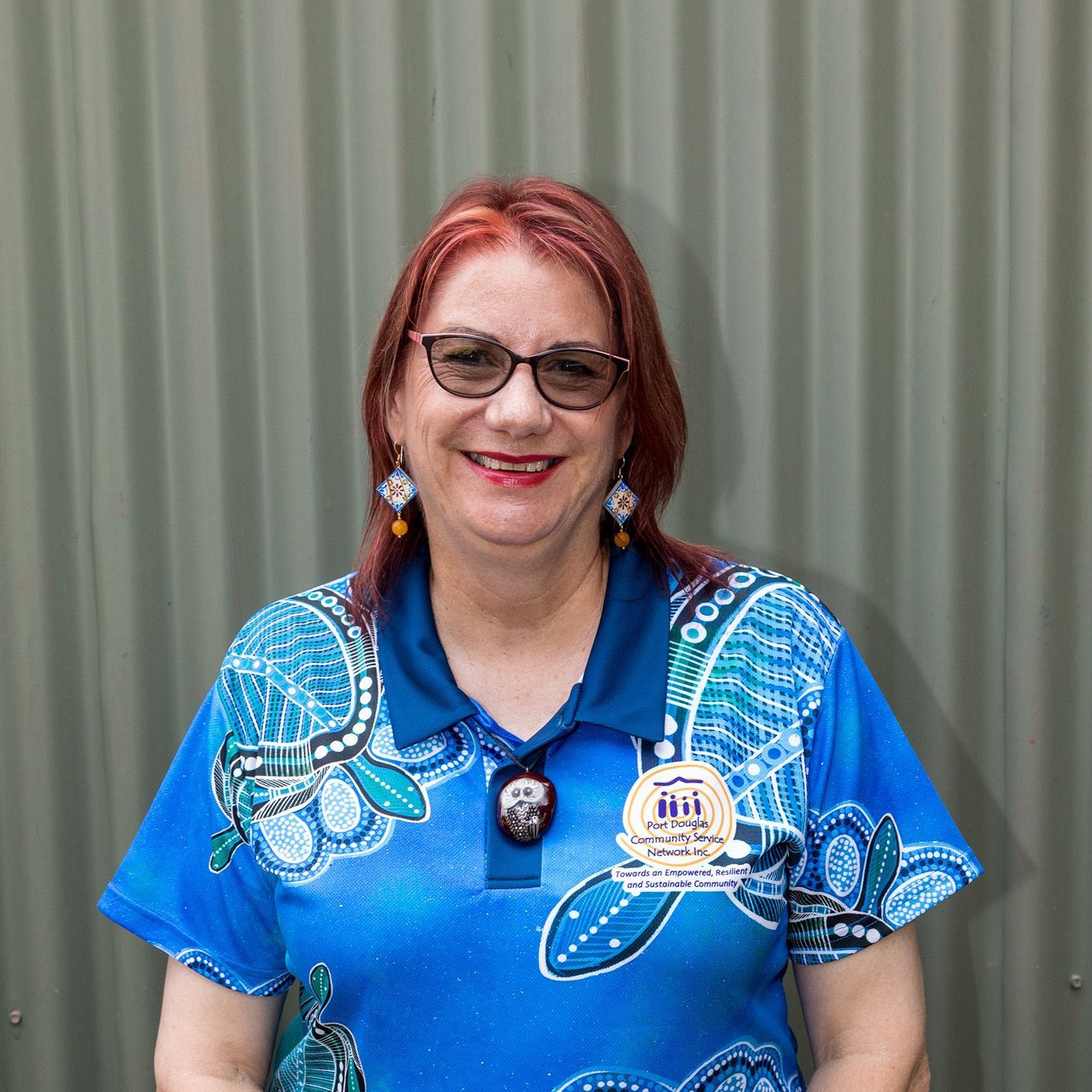 A woman wearing glasses and a blue shirt is standing in front of a wall.