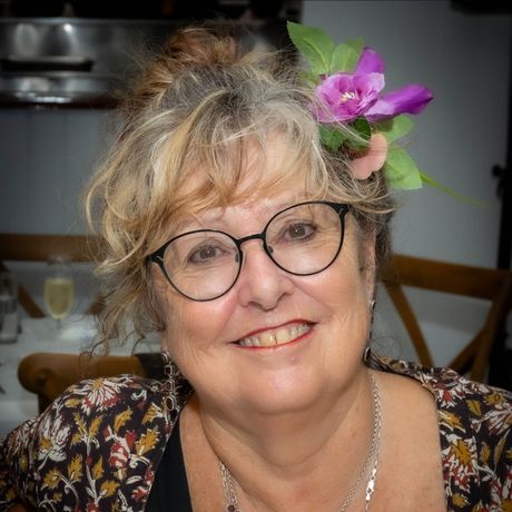 A woman wearing glasses and a flower in her hair is smiling.