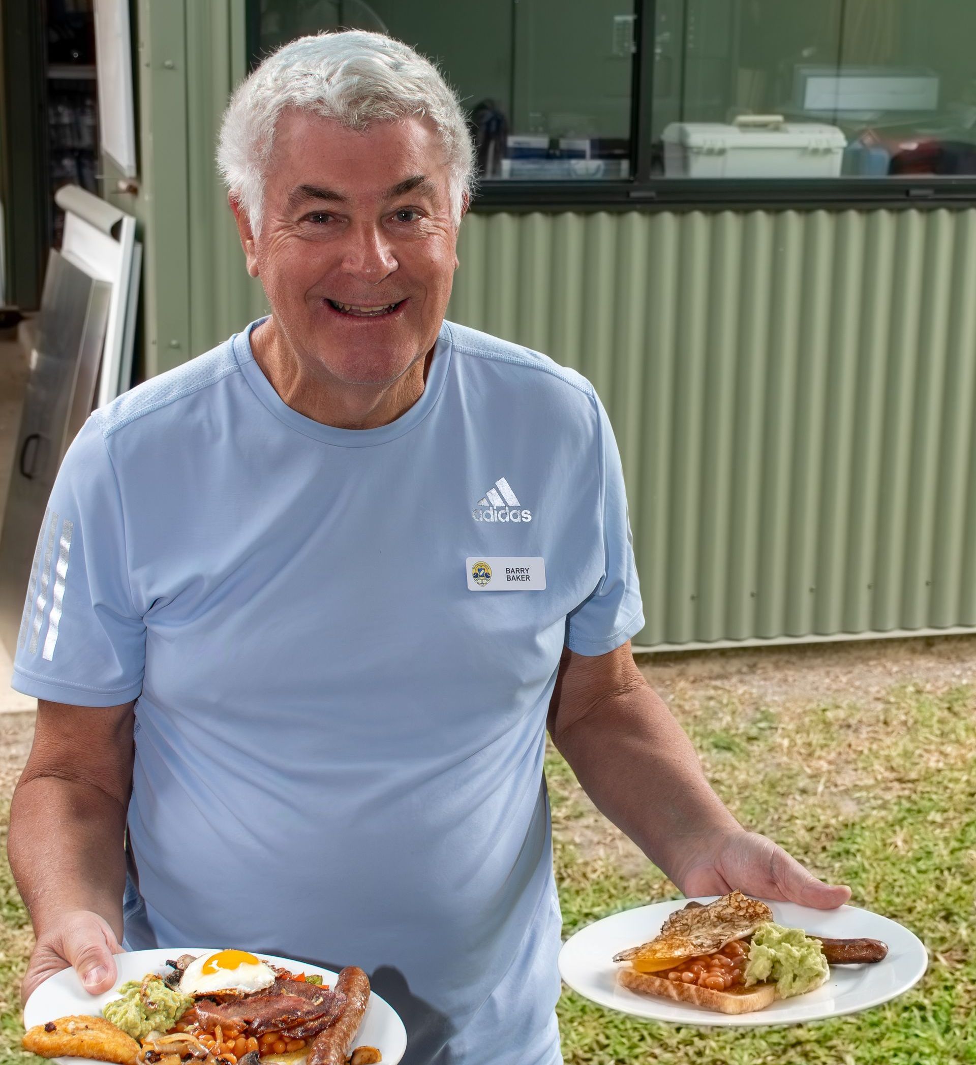 A man in a blue adidas shirt is holding two plates of food