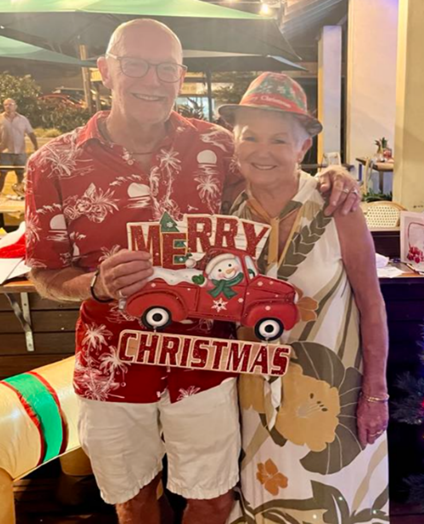 A man and woman are holding a merry christmas sign
