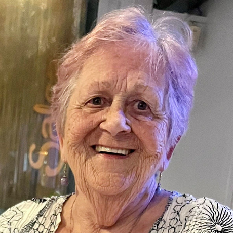 Smiling woman with pinkish hair, wearing a patterned blouse.