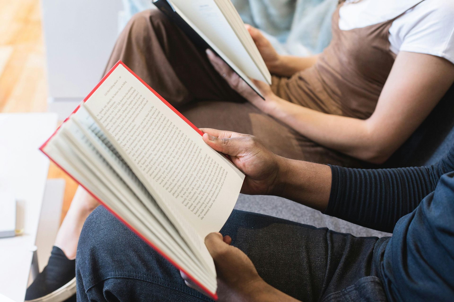 A man and a woman are sitting on a couch reading books.