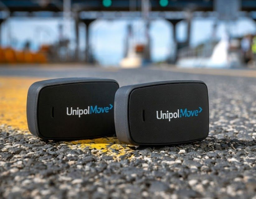 Due transponder UnipolMove per il pagamento del pedaggio su una strada vicino a caselli sfocati e segnali aerei