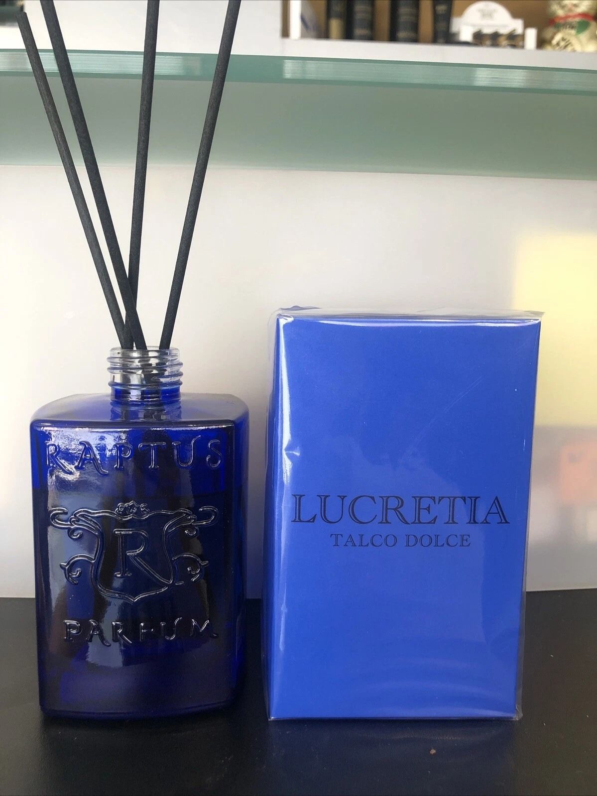 Flacone diffusore di profumo blu con bastoncini, accanto a una scatola coordinata di Eau de Parfum LUCREZIA.