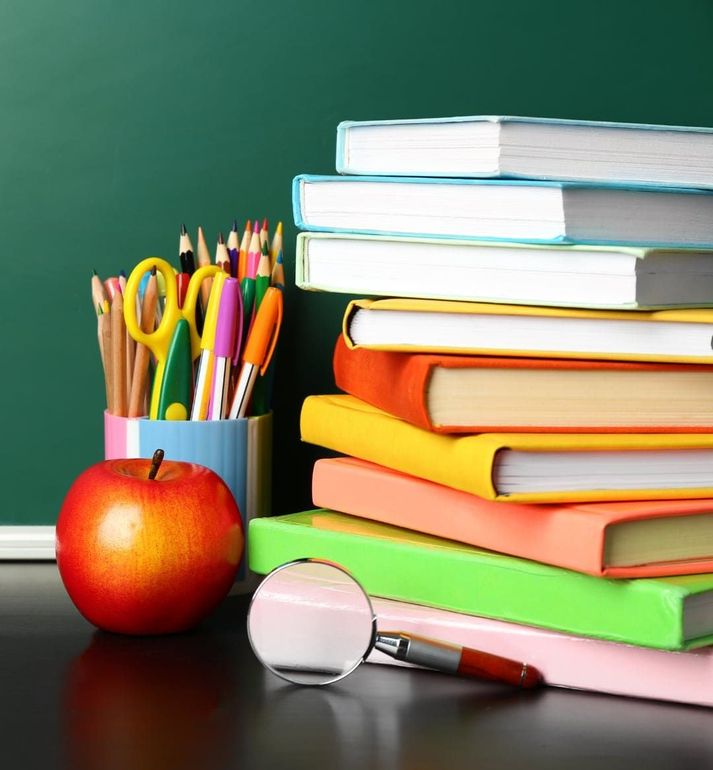 Una pila di libri colorati con matite in un bicchiere, una mela e degli occhiali su una scrivania, su uno sfondo verde.
