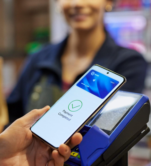 Una mano che tiene uno smartphone sopra un terminale di pagamento blu, mostrando la schermata di avvenuto pagamento contactless.