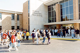 Students leaving Antioch Community High School. Exterior shot of a school building with a crowd exiting the front doors.