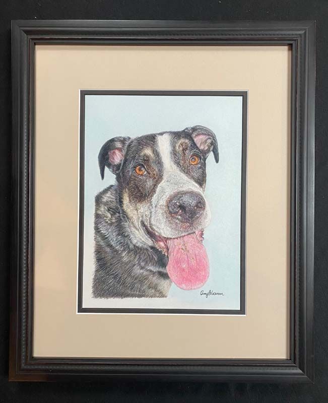 Framed portrait of a black-and-white dog with a pink tongue on a cream mat
