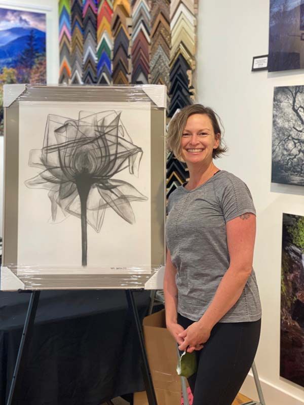 Woman smiling beside abstract charcoal drawing in an art gallery.