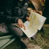 Person sitting in a tent, studying a folded map by flashlight at a campsite