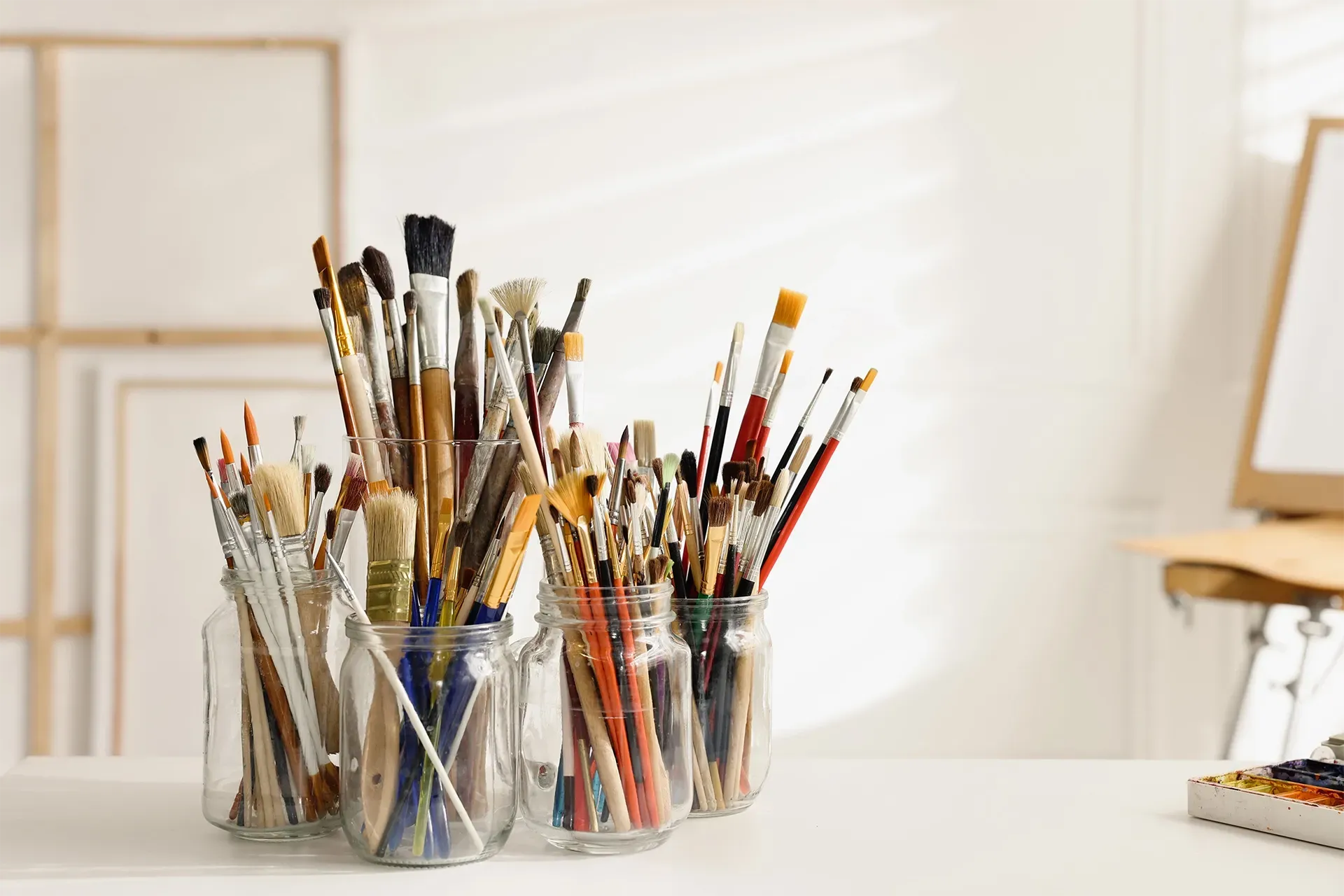 Assorted paintbrushes in glass jars on a bright tabletop in an արվեստ studio