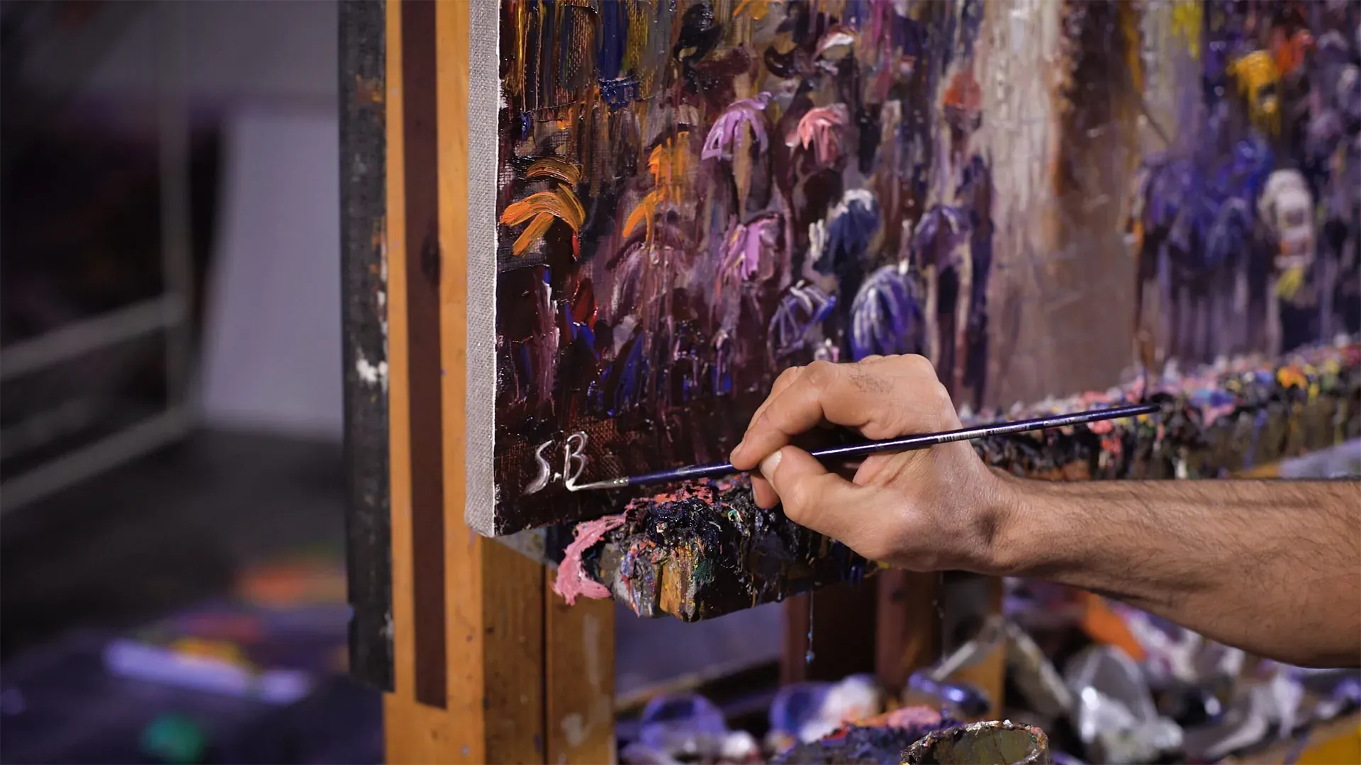 Artist painting an abstract canvas with a brush on an easel, using purple and orange colors.