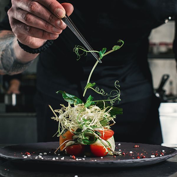 A chef is decorating a plate of food with vegetables and herbs. A chef is decorating a plate of food with vegetables and herbs.