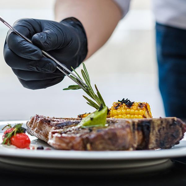 A person wearing black gloves is decorating a plate of food A person wearing black gloves is decorating a plate of food